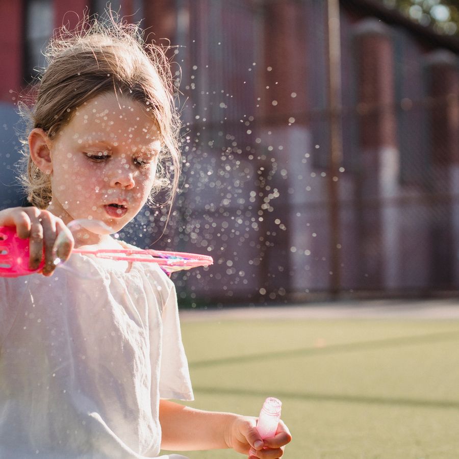 Une enfant fait des bulles de savon dans le jardin.